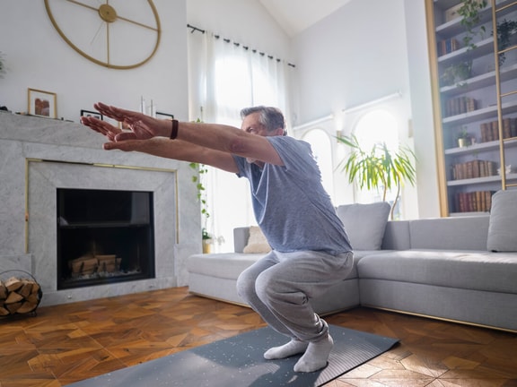 Older adult performing a squat exercise at home for fall prevention, improving strength and balance through evidence-based training.