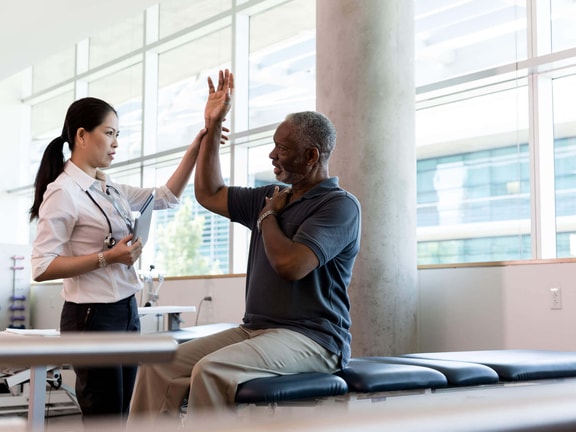 Physical therapist assisting a patient with arm mobility during evaluation for upper extremity osteoarthritis.