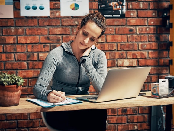 Athletic trainer studying CEU requirements on a laptop and taking notes to prepare for the certification renewal deadline.