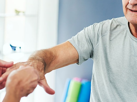 A person helps a senior with arm exercises in a well-lit room at medbridge.