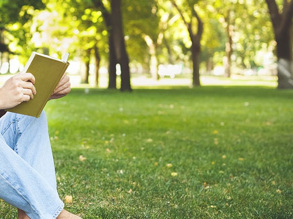 Man sitting by a tree in a park with a notebook, pen, and backpack, suited for medbridge.