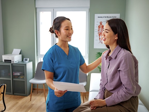 Nurse supporting patient while reviewing the head-to-toe assessment checklist in a clinical exam room.