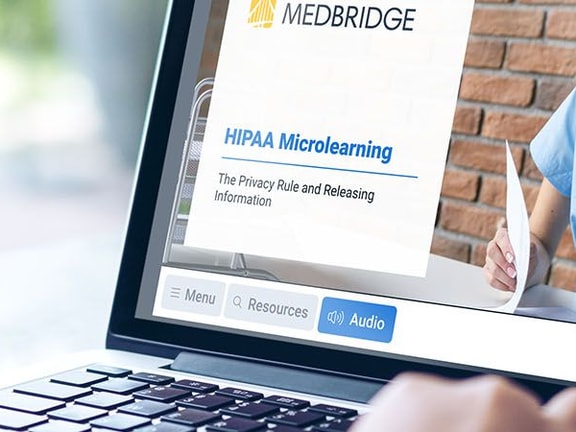 A person uses a laptop showing a medbridge HIPAA Microlearning course featuring a healthcare professional.