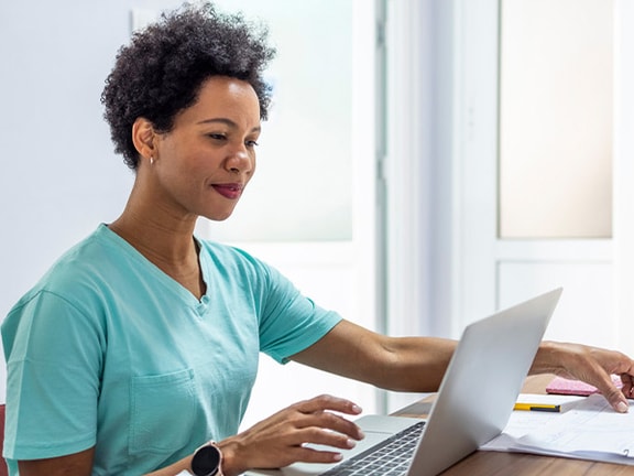 A person in scrubs reviews paperwork on a laptop at a medbridge office desk.