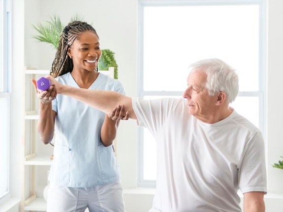 A healthcare provider helps an older man lift a dumbbell, illustrating hybrid care with medbridge.