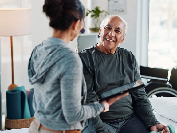 A physical therapist uses a tablet to review a digital home exercise program with a senior Medicare patient during a one-on-one rehabilitation session.