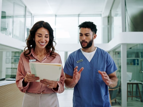 Two healthcare professionals walk through a medical office discussing patient files, highlighting medbridge training.