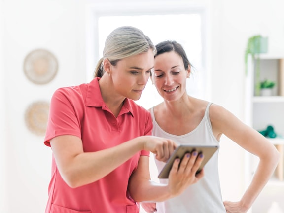 Two women indoors use a tablet, showing how hybrid care with medbridge supports patient interactions.