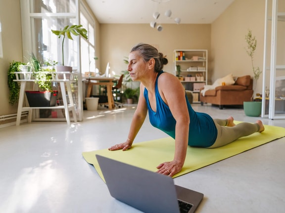 Older woman doing prone press-up exercise on a yoga mat while following a lumbar radiculopathy treatment program online.