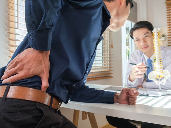 Low back pain consultation in clinic setting, with focus on M54.50 ICD-10 coding and spine-related diagnosis.