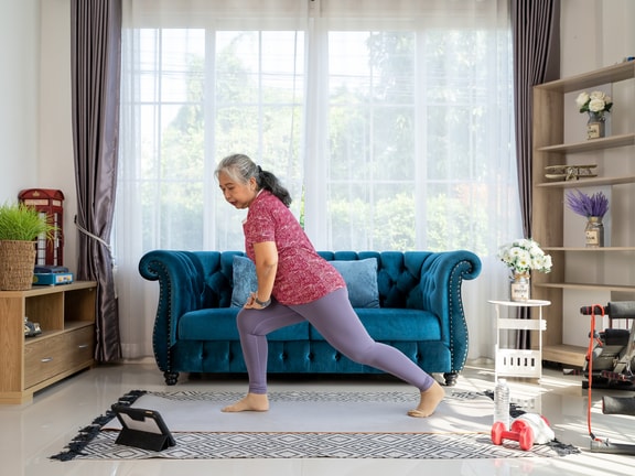 An older adult woman performs her prescribed exercises in her living room.