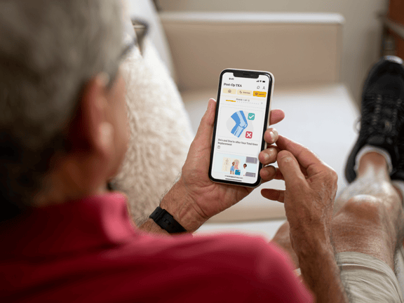 Person on a couch using a smartphone to view a digital healthcare app with medbridge branding visible.