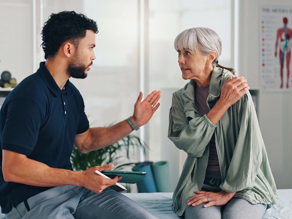 A healthcare worker talks to an elderly woman about hybrid care in a medbridge exam room.