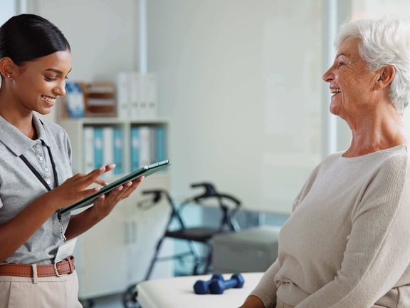 Clinician using remote therapeutic monitoring (RTM) tablet with older patient during outpatient rehabilitation visit