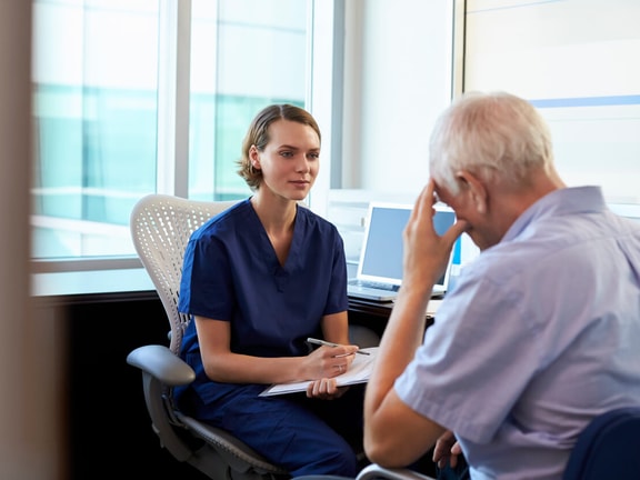 Clinician in scrubs listens attentively to older patient during evaluation, discussing symptoms of cognitive fatigue.