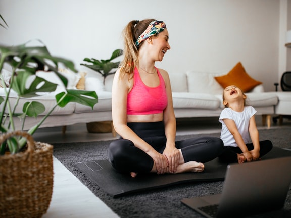 A woman and child laugh while doing yoga with an open laptop in front of them for a medbridge session.