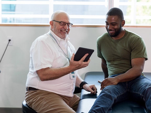 Doctor and patient smile at a tablet in a bright Medbridge exam room.