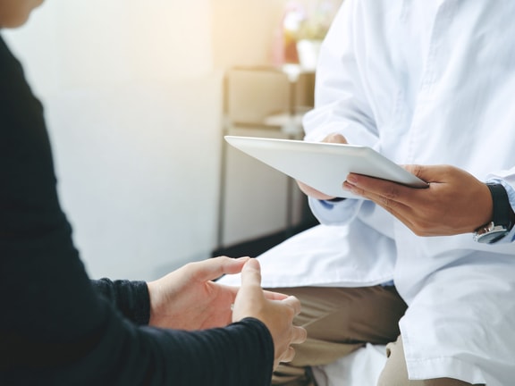 Clinician holds a tablet while consulting with a patient, capturing outcome data during an office visit