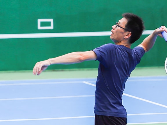 Man in a blue shirt playing tennis on an indoor court, preparing to hit a shot with a racket for medbridge.