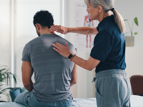 A woman examines a man’s back in a medical office, highlighting digital healthcare and medbridge.