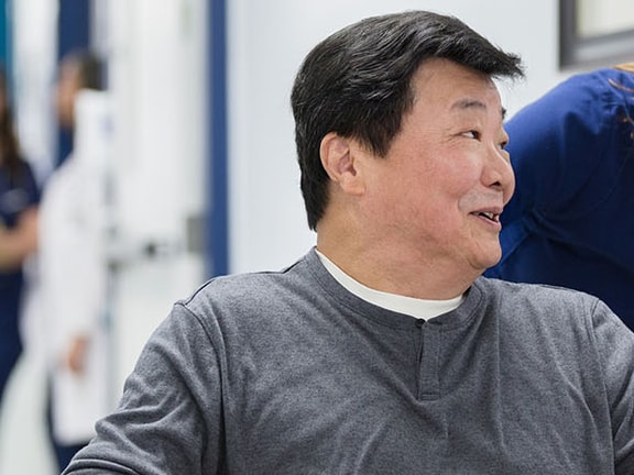 A smiling wheelchair user greets a healthcare worker in a busy medbridge hallway.