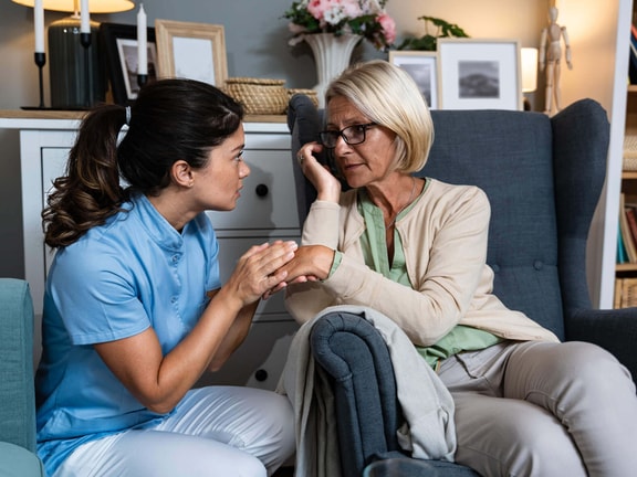 Clinician kneeling beside an older adult, offering calm support during a moment of distress in dementia care.