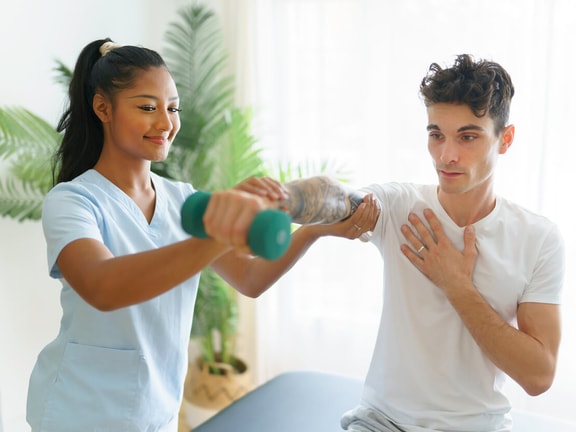 Therapist guiding patient through shoulder rehab exercise for rotator cuff tendinopathy using a dumbbell.