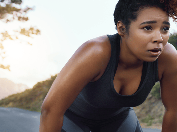 A jogger leans forward to catch her breath on a tree-lined rural road.