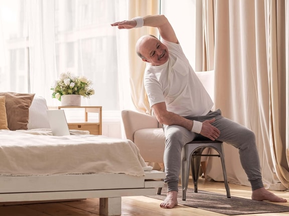 Older adult performing a seated side-bend exercise, illustrating seated balance and postural control assessed by the Sitting Balance Scale.