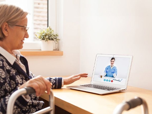 An elderly woman in a wheelchair video calls a healthcare professional on a medbridge laptop.