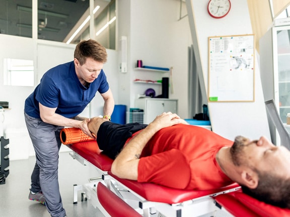 Clinician applying sports manual therapy with foam roller to athlete’s knee during rehab session.