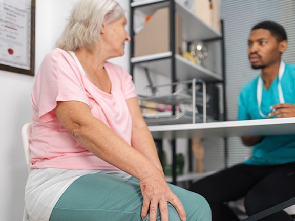 An older woman consults with a Medbridge professional in teal scrubs at a medical office.