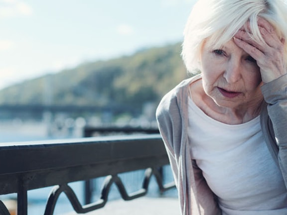 Person leaning on a railing outdoors, holding their head and appearing distressed.