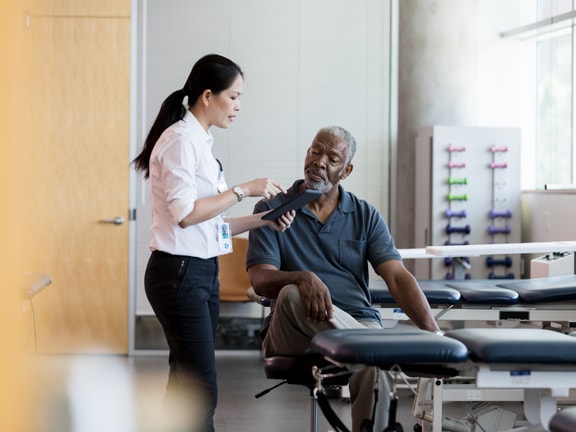A healthcare worker helps an older man put on a wrist brace in a medbridge clinic, demonstrating patient care.