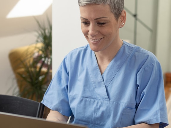 A person in blue scrubs works on a laptop at a desk, with Medbridge materials visible.