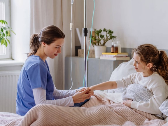 A home health nurse providing bedside care to a pediatric patient during an in-home visit.