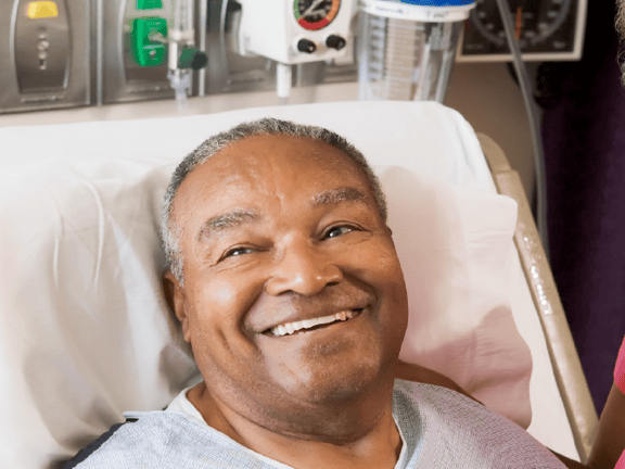 A Medbridge patient in bed smiles at a doctor and a woman.