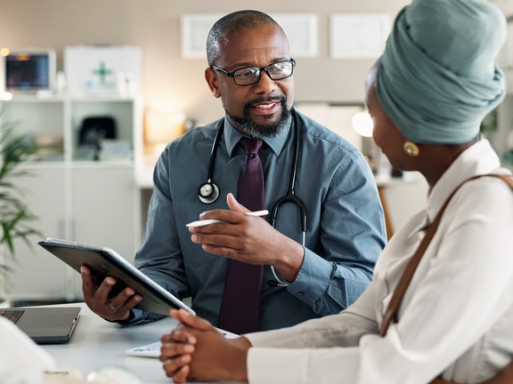 A healthcare worker shows a woman in a headscarf how to use medbridge on a tablet.