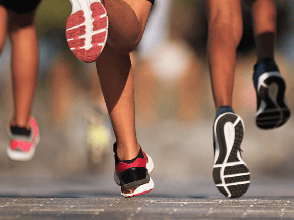Group of runners' legs and sneakers moving on a paved road.