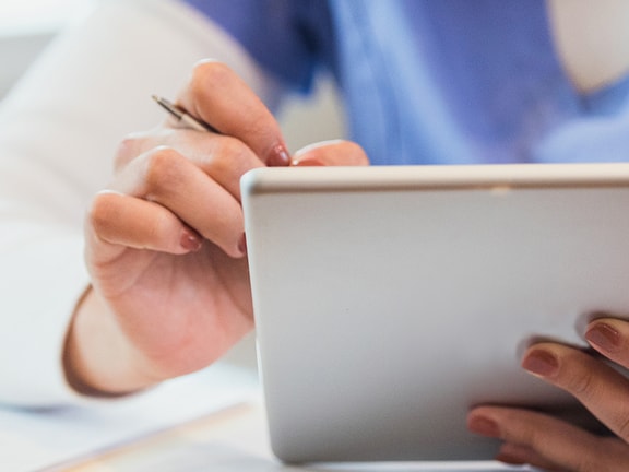 A Medbridge employee in a blue uniform uses a tablet with a stylus.