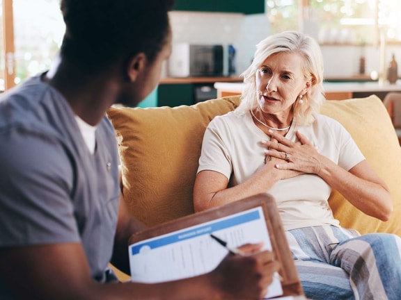 An elderly woman talks with a healthcare worker using Medbridge software and writing notes.