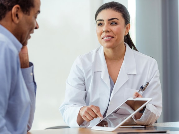 Orthopedic clinician reviews patient-reported outcome results on a tablet with a joint replacement patient during a follow-up visit.