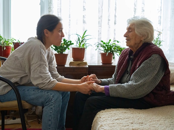 A younger woman holds hands with an older woman in a bright, plant-filled room, showing medbridge's patient care focus.