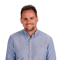Man smiling in a light blue shirt with short hair and beard, standing against a white background (medbridge).
