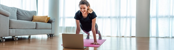 Individual doing a workout on a pink yoga mat with a laptop in a bright living room, following medbridge instructions.