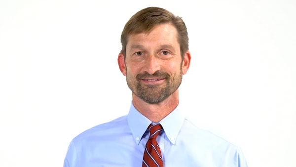 Man with short brown hair and beard in a blue shirt and red striped tie, smiling slightly against a white background for medbridge.