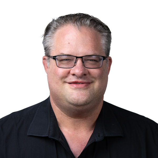 Smiling man with short gray hair and glasses in a black collared shirt stands before a white background; he works on digital healthcare at medbridge.