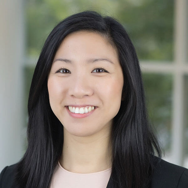 Woman in a black blazer with long black hair, smiling indoors.