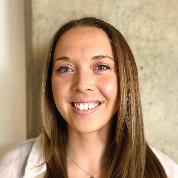 A person with long brown hair smiling in front of a textured wall for medbridge.