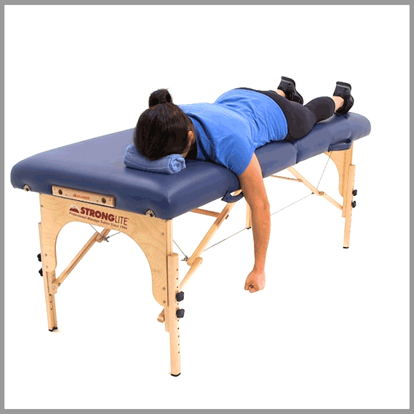 Individual in a blue shirt and black pants lying face down on a blue massage table, arms hanging.